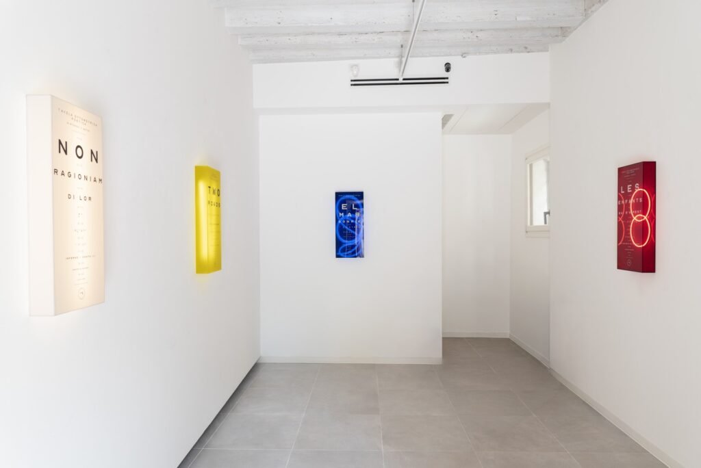The corridor of Marignana Project with four illuminated lightboxes in cream, yellow, blue and red along the walls