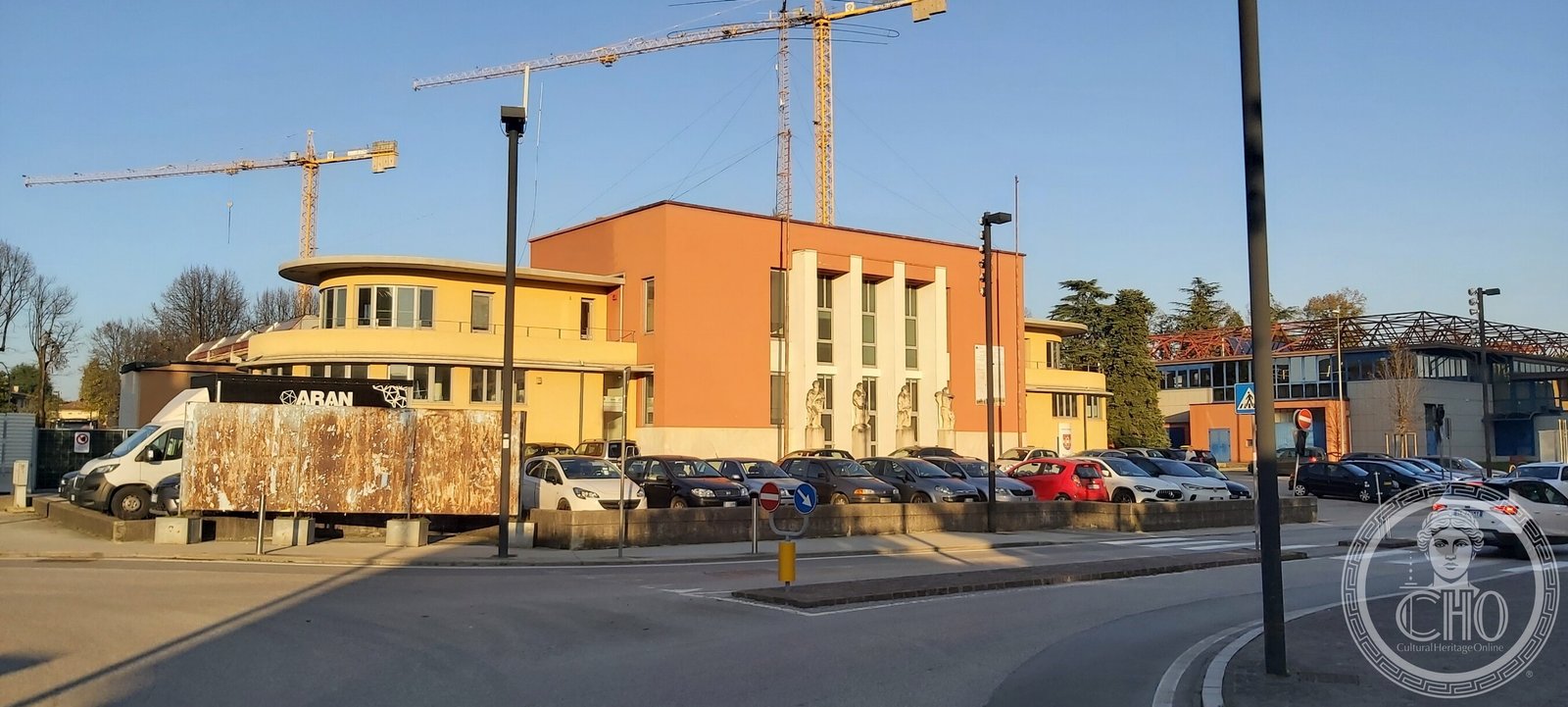 Three-quarter view of the former Casa del Balilla showing one curved yellow wing with ribbon windows against the red central block