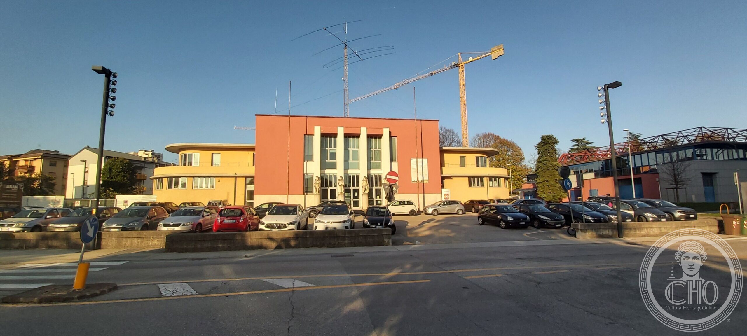 The former Casa del Balilla in Pordenone: a red rendered central block with a giant order of white pilasters, flanked by two low curved wings in yellow