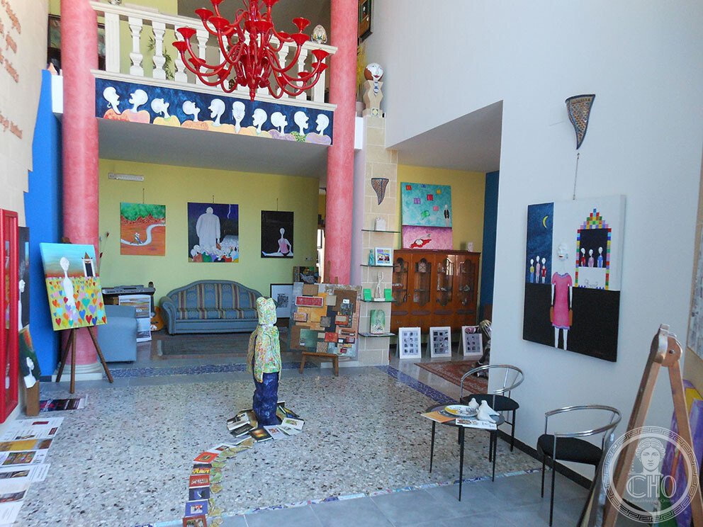 The double-height gallery of the Casa degli Artisti with pink columns and red chandelier