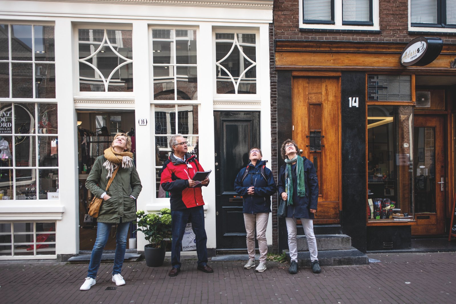 Three walkers and their guide looking up at the gables above the shopfronts on an Amsterdam street