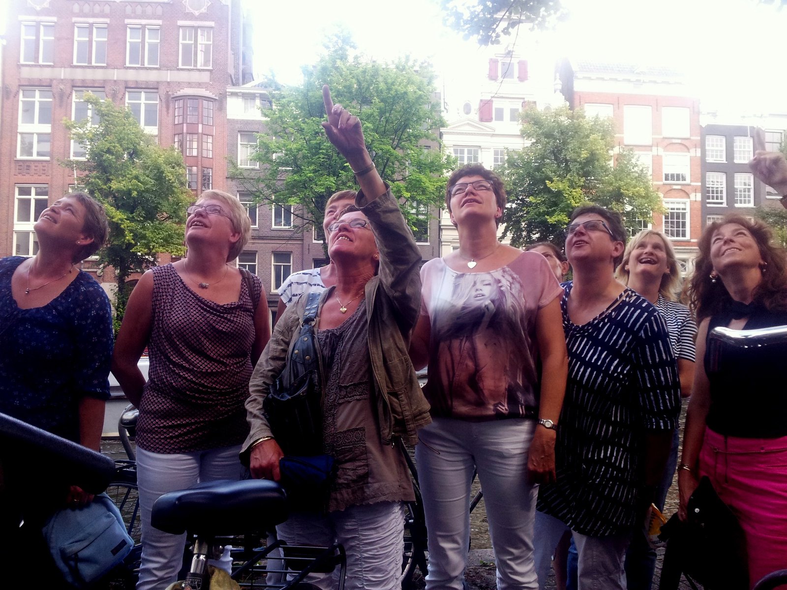 A group of walkers looking upward as their guide points at a canal house facade in Amsterdam