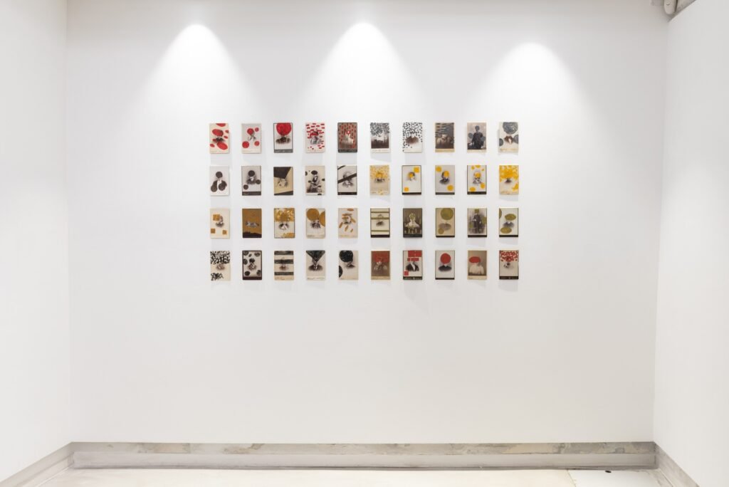 A wall hung with a grid of about forty small works, each a photographic portrait partly covered by painted marks