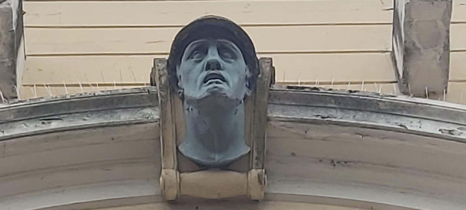Bronze keystone mask of a helmeted soldier with upturned face and open mouth on the Casa del Mutilato in Padua
