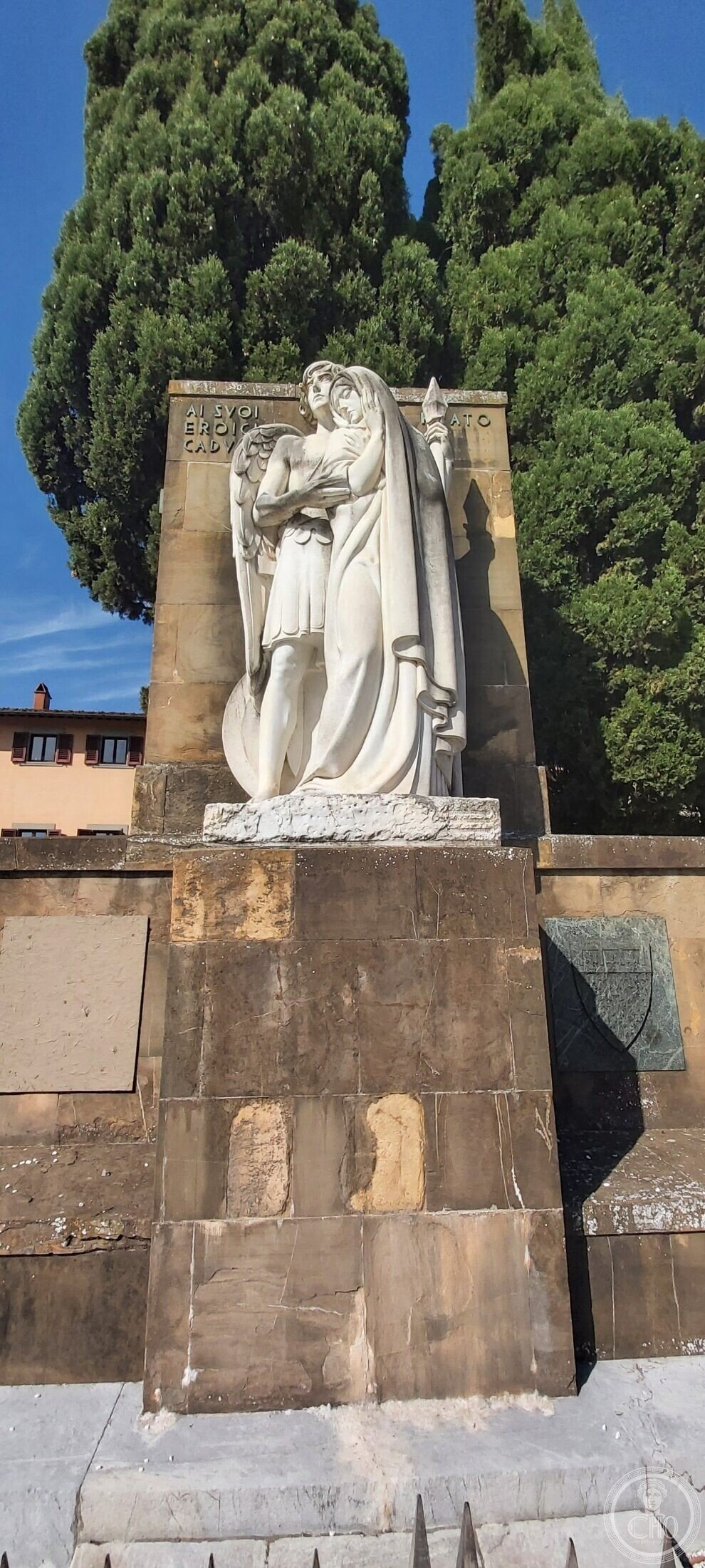 The marble group of the Prato war memorial: a winged youth supporting a veiled figure with clasped hands, against a stone stele inscribed AI SVOI EROICI CADVTI