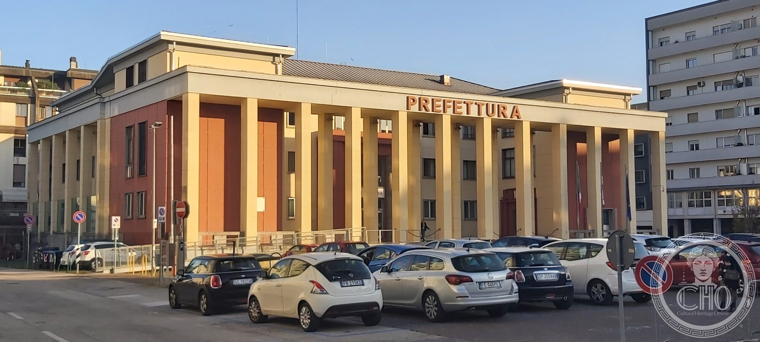 The Prefecture of Pordenone, former Casa del Fascio: a raised block with a giant order of square pilasters in pale render over red ribbed facing, lettered PREFETTURA