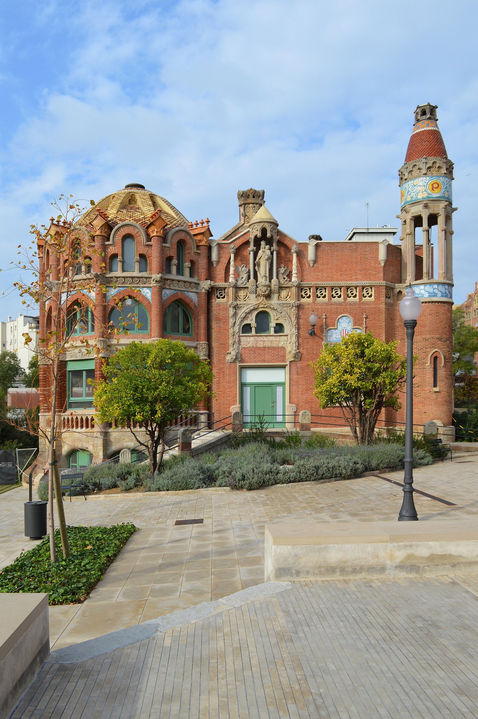 A restored brick pavilion at Sant Pau with a tiled dome and a ceramic tower, seen across the gardens