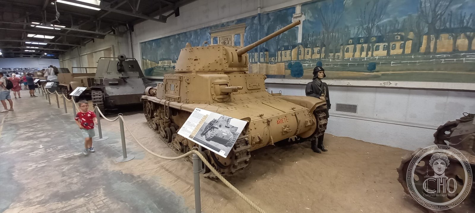 The M15/42 in the museum hall beside other vehicles, with a visitor and a uniformed mannequin for scale