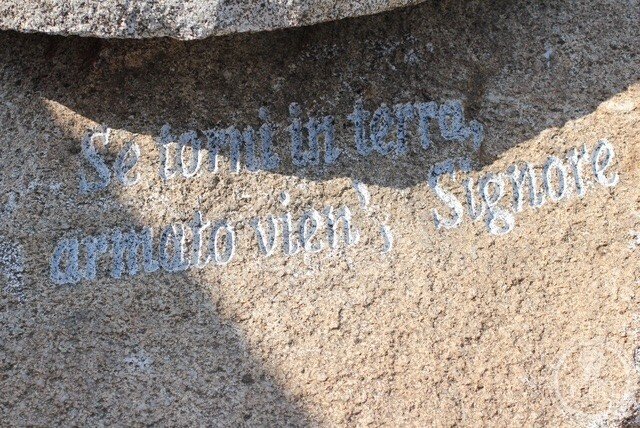 A line of verse cut in cursive letters into the granite: Se torni in terra, armato vien', Signore