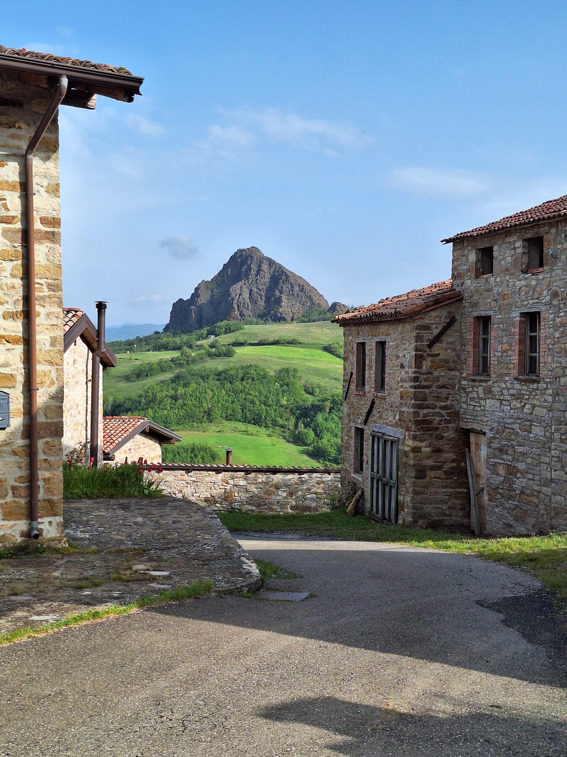 Borgo di Travo — stone lane opening onto green pastures with the peak of Pietra Parcellara
