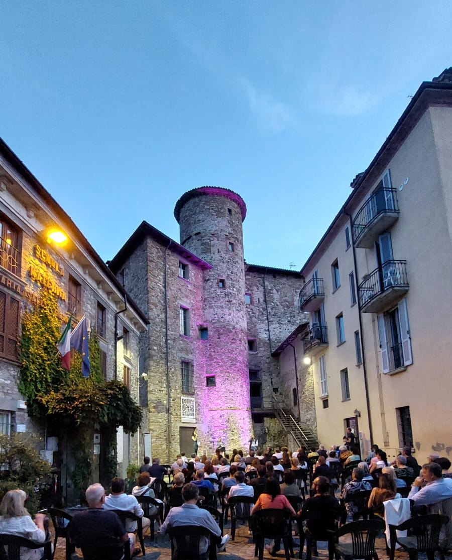 Castello Anguissola Travo — the piazzetta under the round tower at dusk, audience seated for a reading