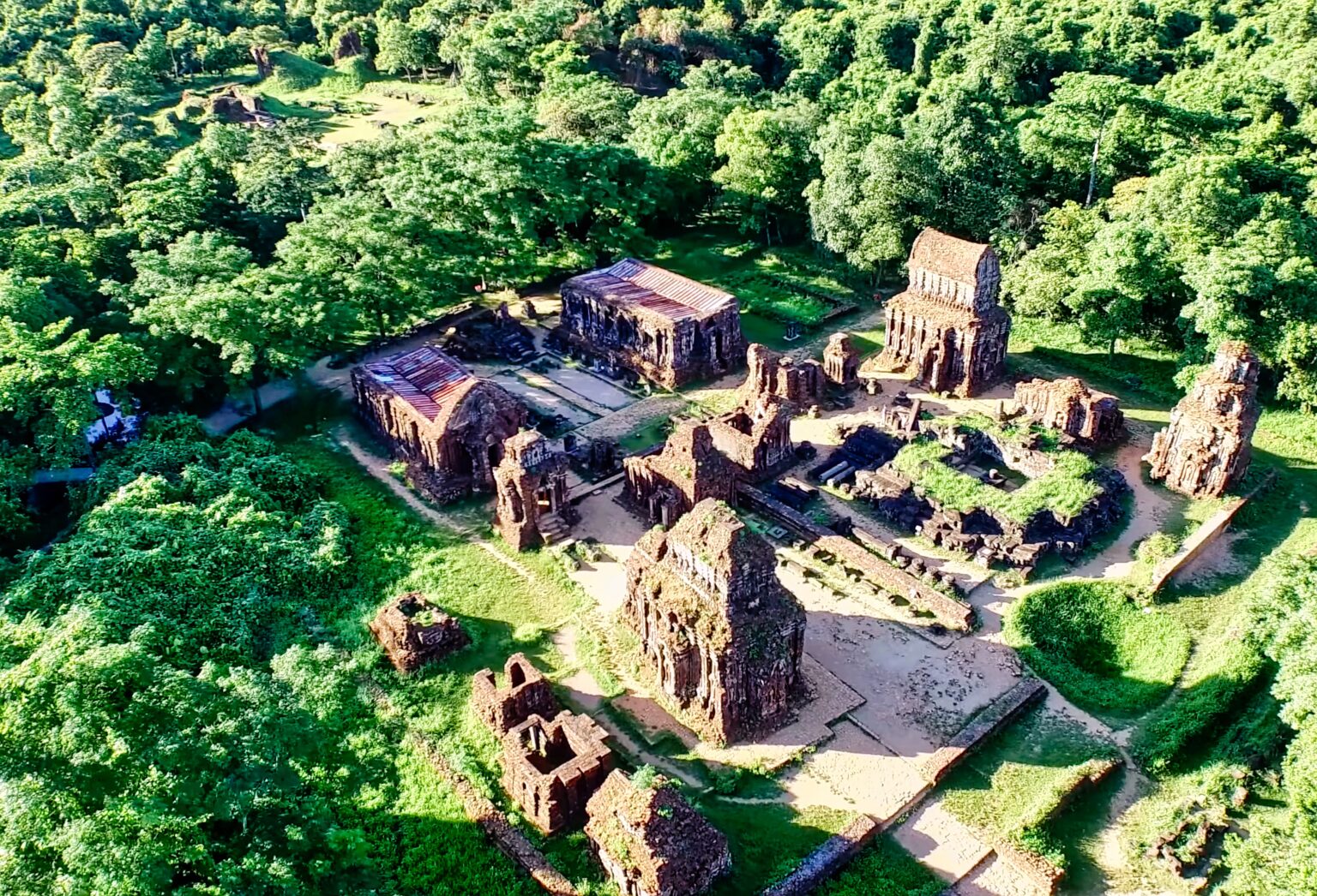 An aerial view of the brick temple groups at Mỹ Sơn standing in clearings surrounded by dense green forest