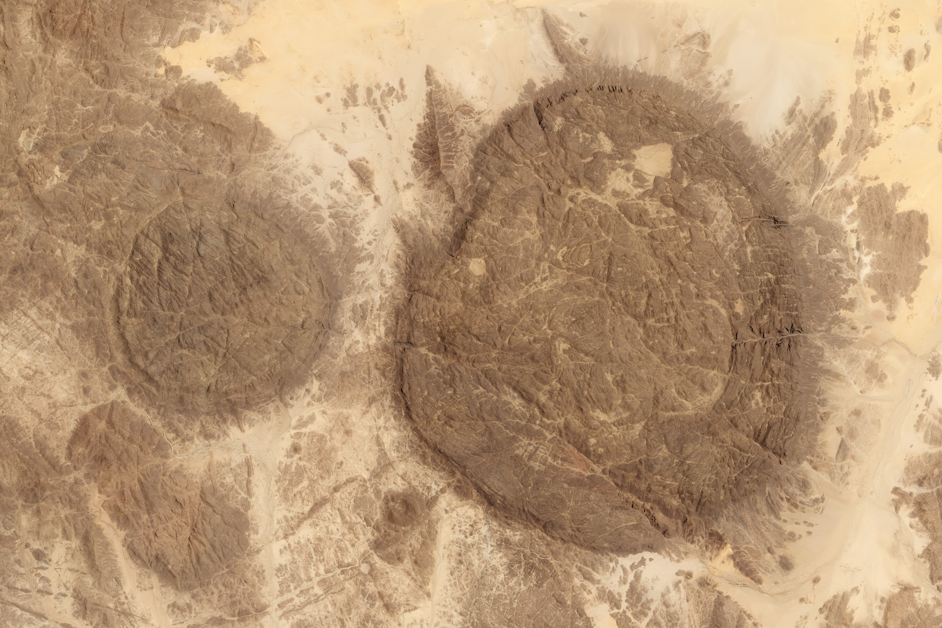 Aïr Mountains dark volcanic domes rising from the tan Sahara Desert, Niger, seen from orbit