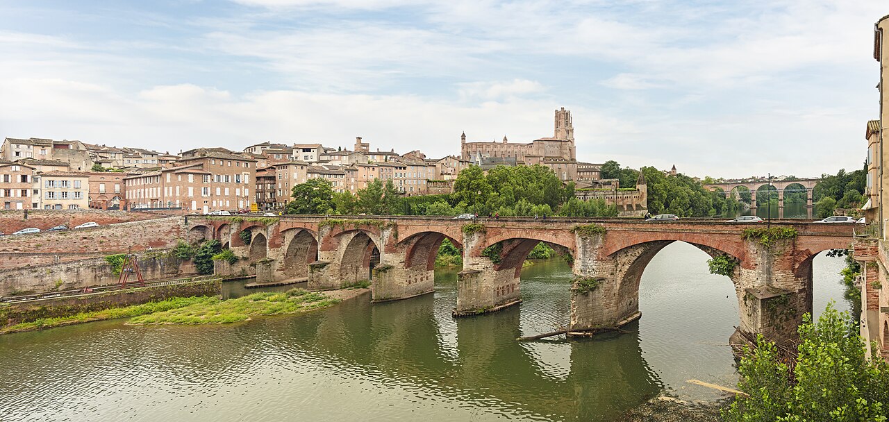Aerial view of Albi showing the fortified Sainte-Cécile Cathedral — the world's largest brick cathedral — rising above the Tarn river and the 11th-century Pont Vieux, with the Bishop's Palace on the left