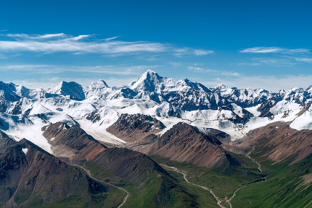 Snow-covered peaks of the Tianshan (Tien Shan) mountain range above green alpine meadows in Khan Tengri Nature Park, Xinjiang, China — part of the UNESCO-inscribed Xinjiang Tianshan World Heritage Site