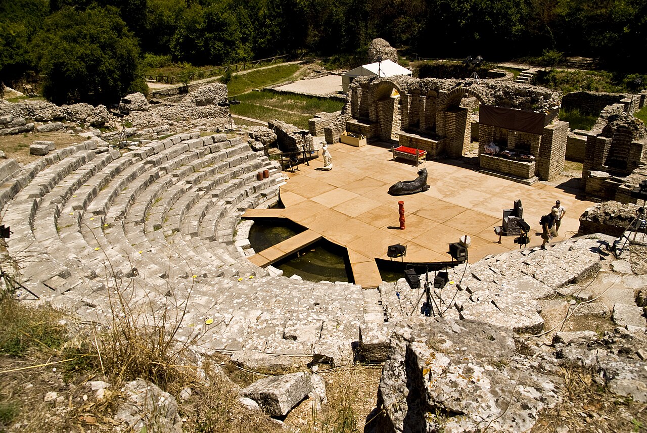 The ancient theatre of Butrint (3rd century BCE), its limestone cavea seats rising in a natural hollow of the forested hillside above the Vivari Channel in southern Albania