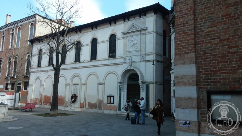 St George's Anglican Church seen from the campo, its white front beside a brick building, people walking past the door