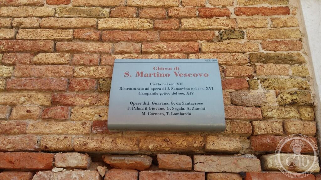 A stone plaque on the brick wall of the church of San Martino in Venice, giving its dates and the names of the artists whose work is inside