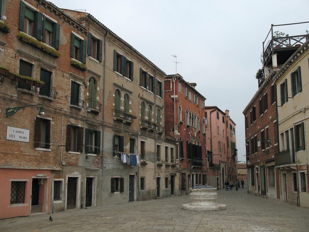 A Venetian square with a stone wellhead, brick houses and a street sign reading Campo dei Mori