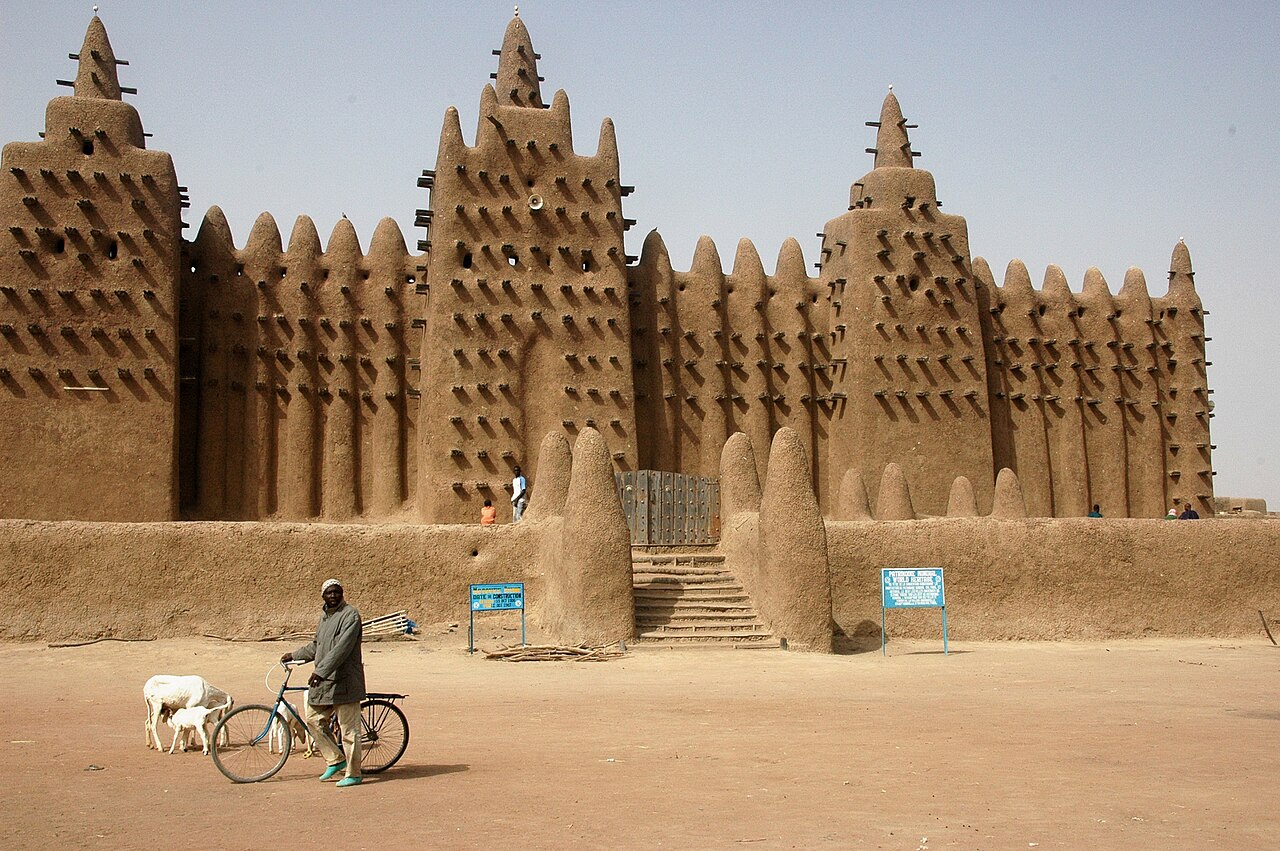 The Great Mosque of Djenné, Mali — the world's largest mud-brick building, a Sudano-Sahelian mosque with three minarets bristling with torons (wooden structural rods), photographed from the market square