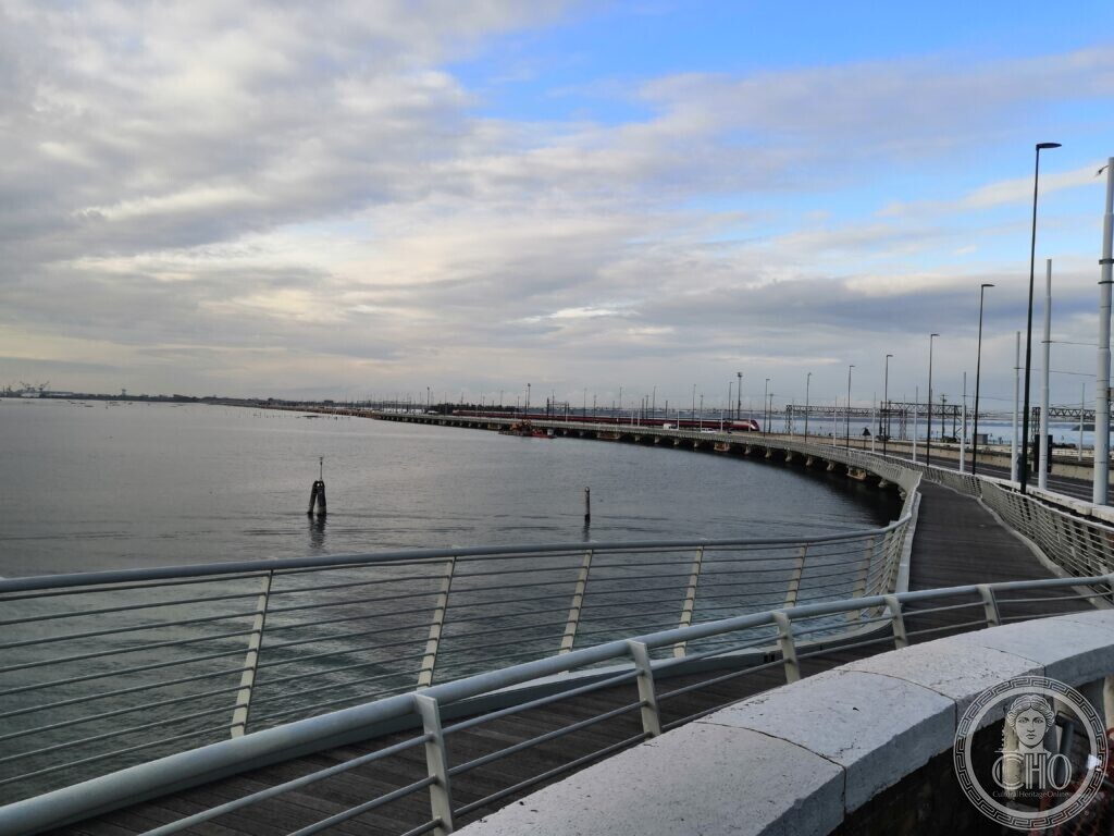 The Ponte della Libertà seen along its stone parapet, lamp posts marching across the lagoon and the railway line beside the road