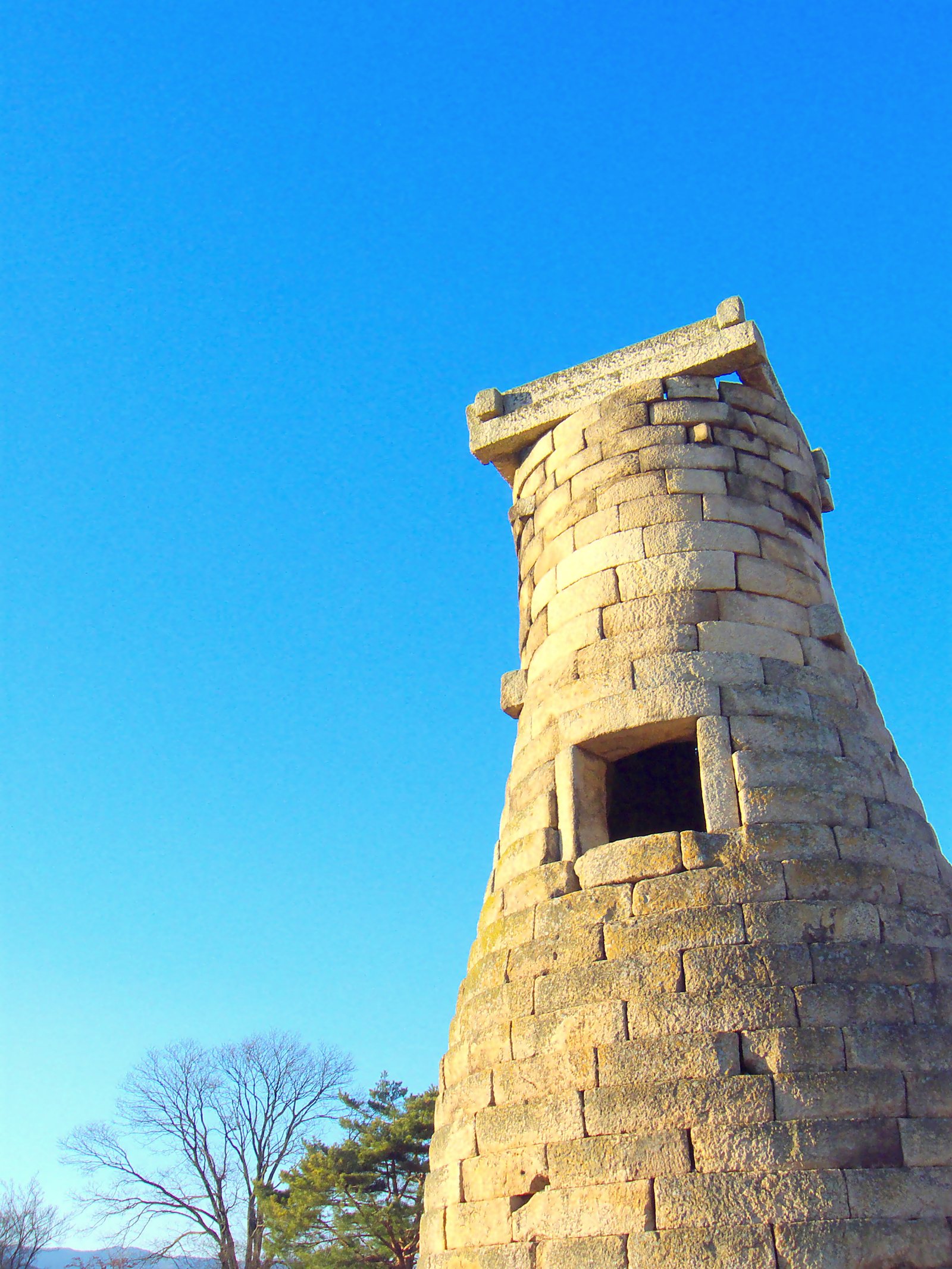 Cheomseongdae observatory in Gyeongju, a rounded stone tower of stacked granite blocks standing in a green field under blue sky