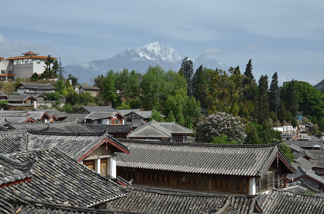 Cobblestone street in the Old Town of Lijiang with traditional Naxi wooden architecture and the snow-capped Jade Dragon Snow Mountain visible in the background