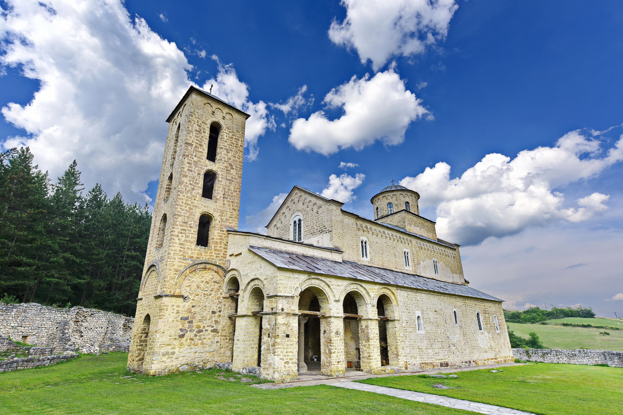 Exterior of Sopoćani monastery with stone bell tower in wooded hillside landscape