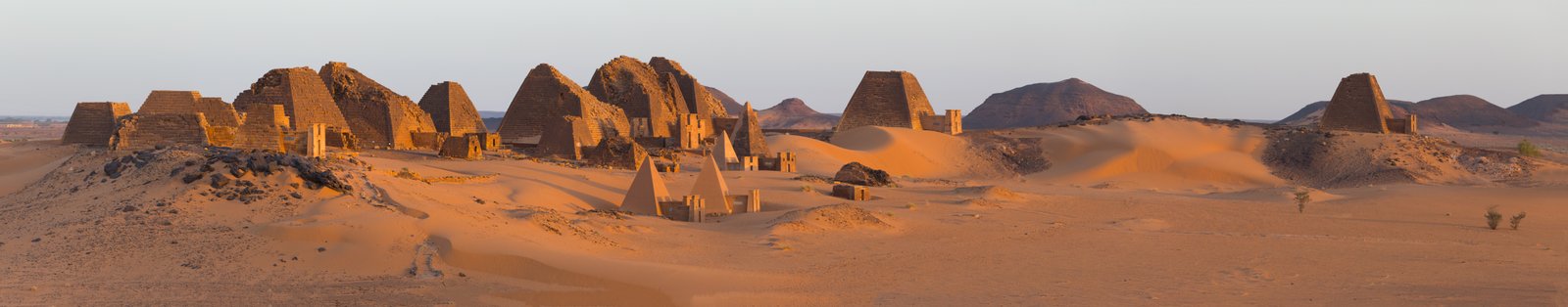 Panoramic view of Meroe pyramids glowing amber at sunrise in the Nubian desert