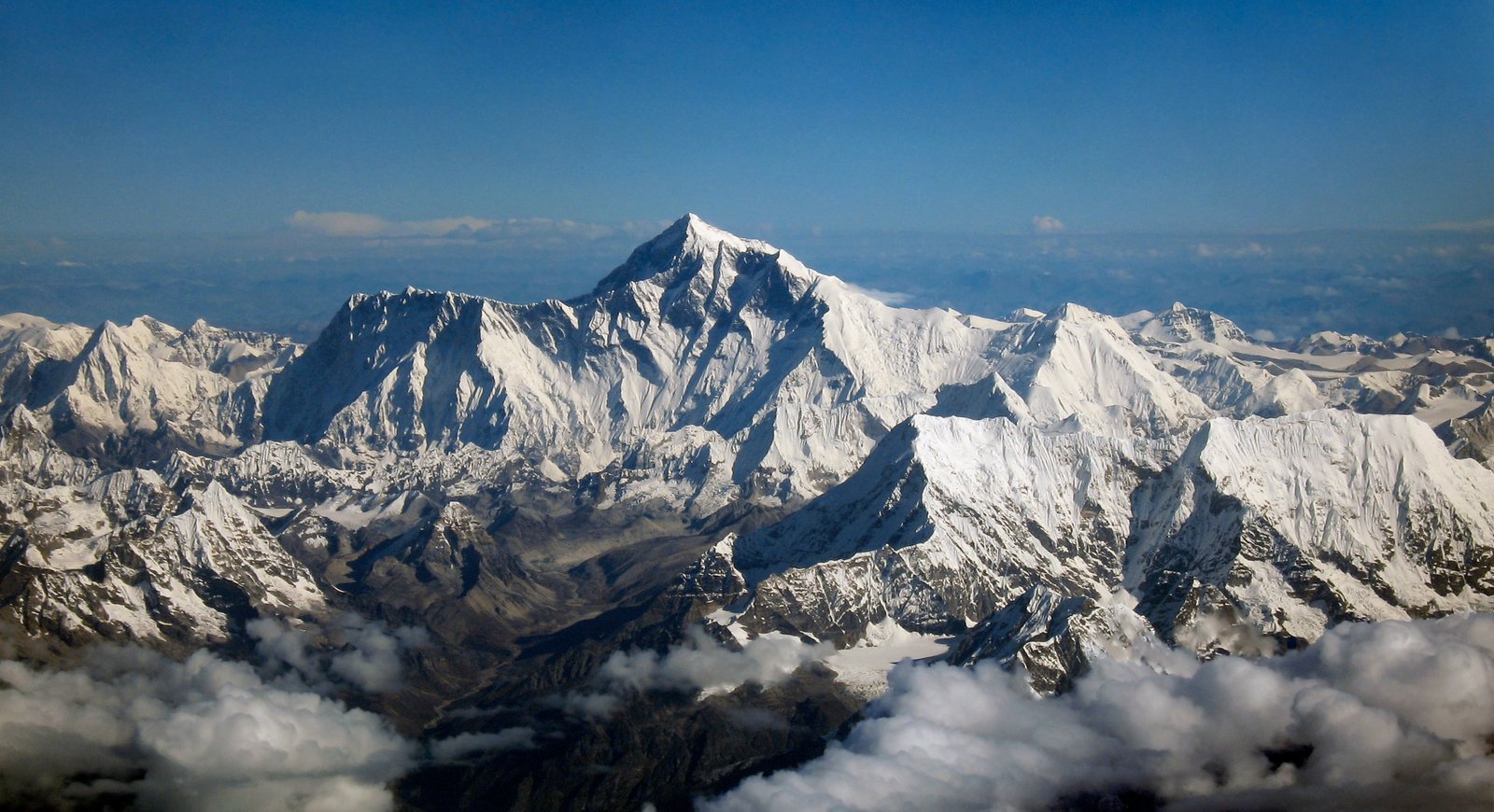 Mount Everest summit pyramid rising above cloud and glaciated Himalayan ridgelines from the air