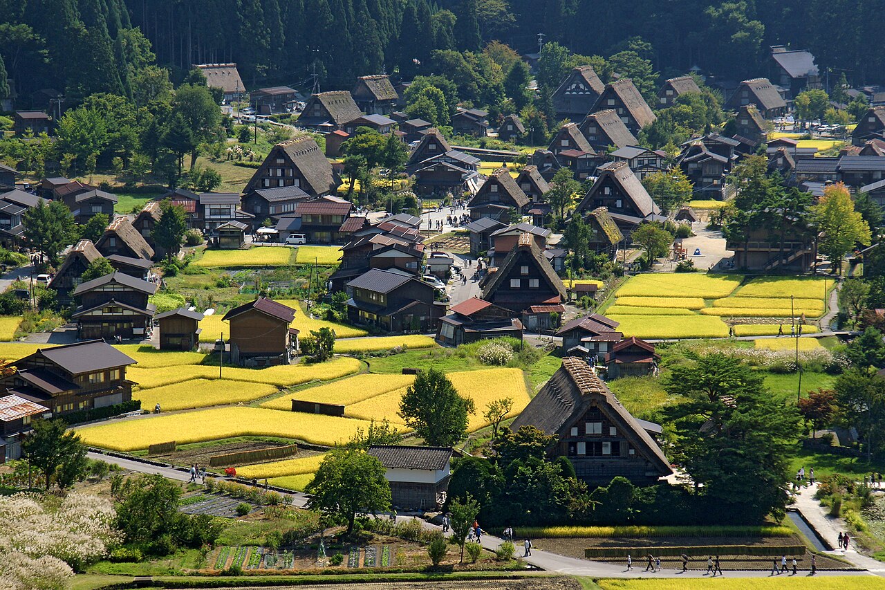 Traditional gasshō-zukuri farmhouses in Ogimachi, Shirakawa-gō, Gifu prefecture, Japan — steep thatched roofs designed to shed the region's heavy winter snowfall, with the Shō River valley and surrounding mountains