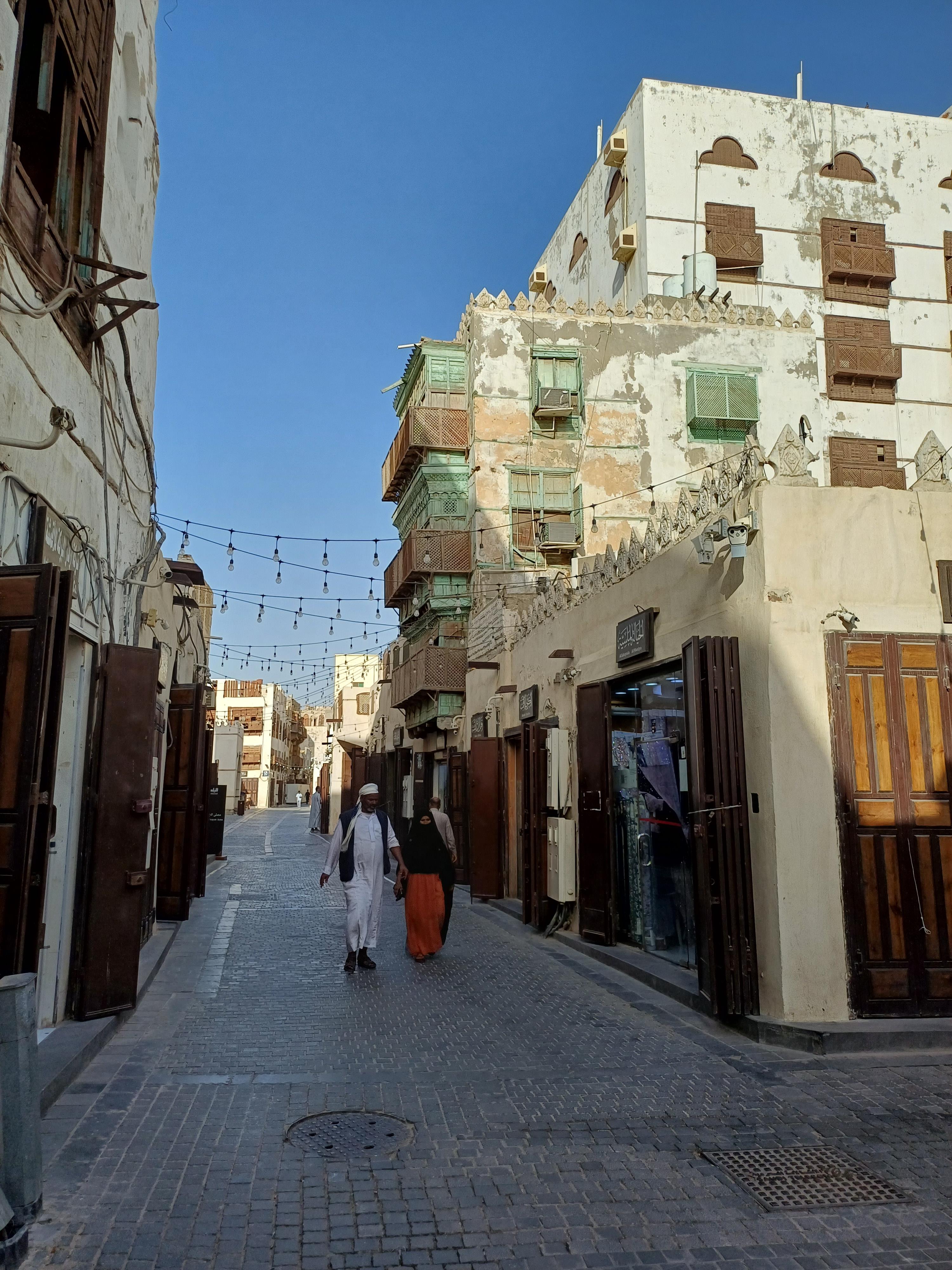 Narrow lane flanked by coral-stone tower houses with carved wooden mashrabiyya screens in old Jeddah
