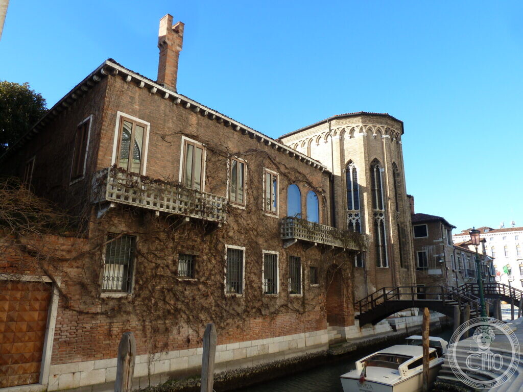 The abbey buildings of San Gregorio along the canal, a stone balcony hung with creeper, the Gothic apse rising behind them