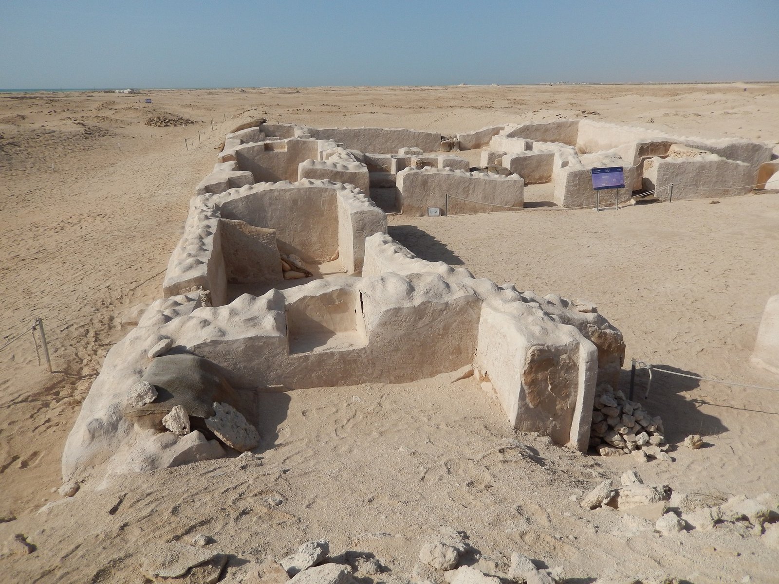Partially restored stone walls of the ruined town of Zubarah under a wide desert sky