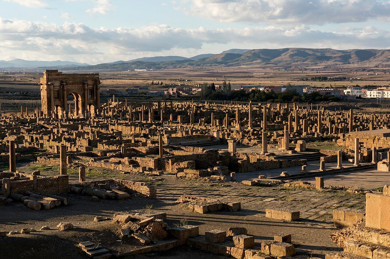 Aerial view of Timgad Roman colony ruins on the Algerian steppe, showing the perfect orthogonal street grid of the cardo and decumanus with the triumphal arch visible at the western entrance