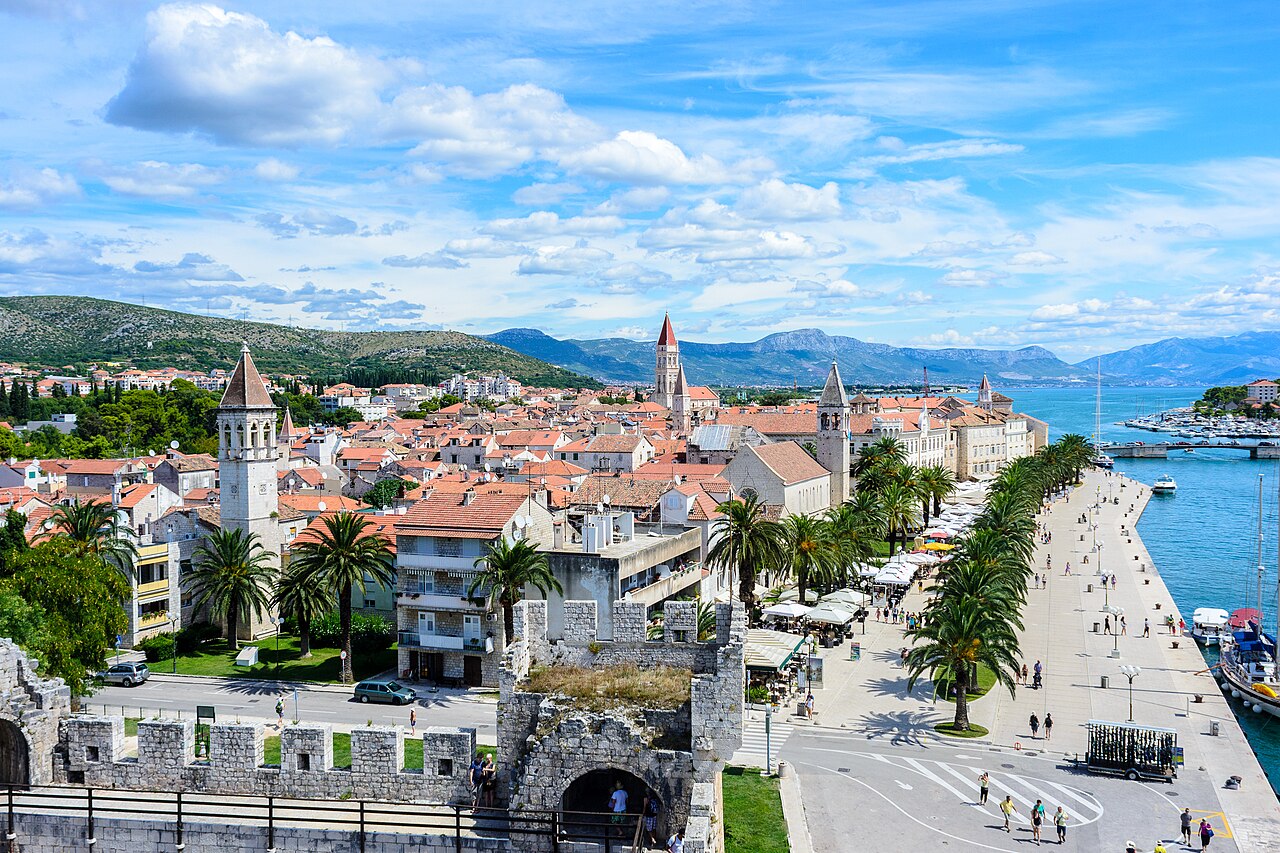 Aerial view of the Historic City of Trogir, Croatia — the small island city connected to the mainland by a bridge and to Čiovo Island by another bridge, its compact medieval grid of Romanesque and Gothic streets and buildings surrounded by intact walls on three sides by the Adriatic Sea, a UNESCO World Heritage Site inscribed in 1997 as the best-preserved Romanesque-Gothic city in Europe