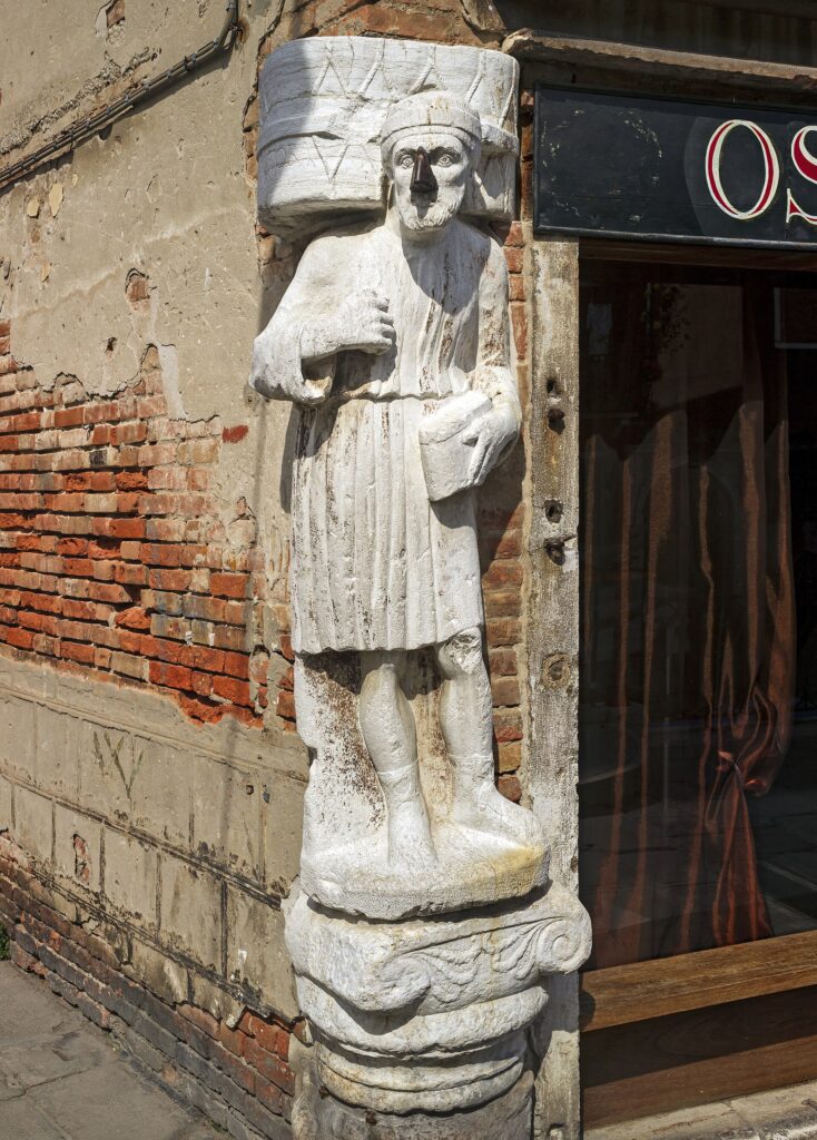 A weathered stone figure in eastern dress set into a brick corner, its nose made of iron