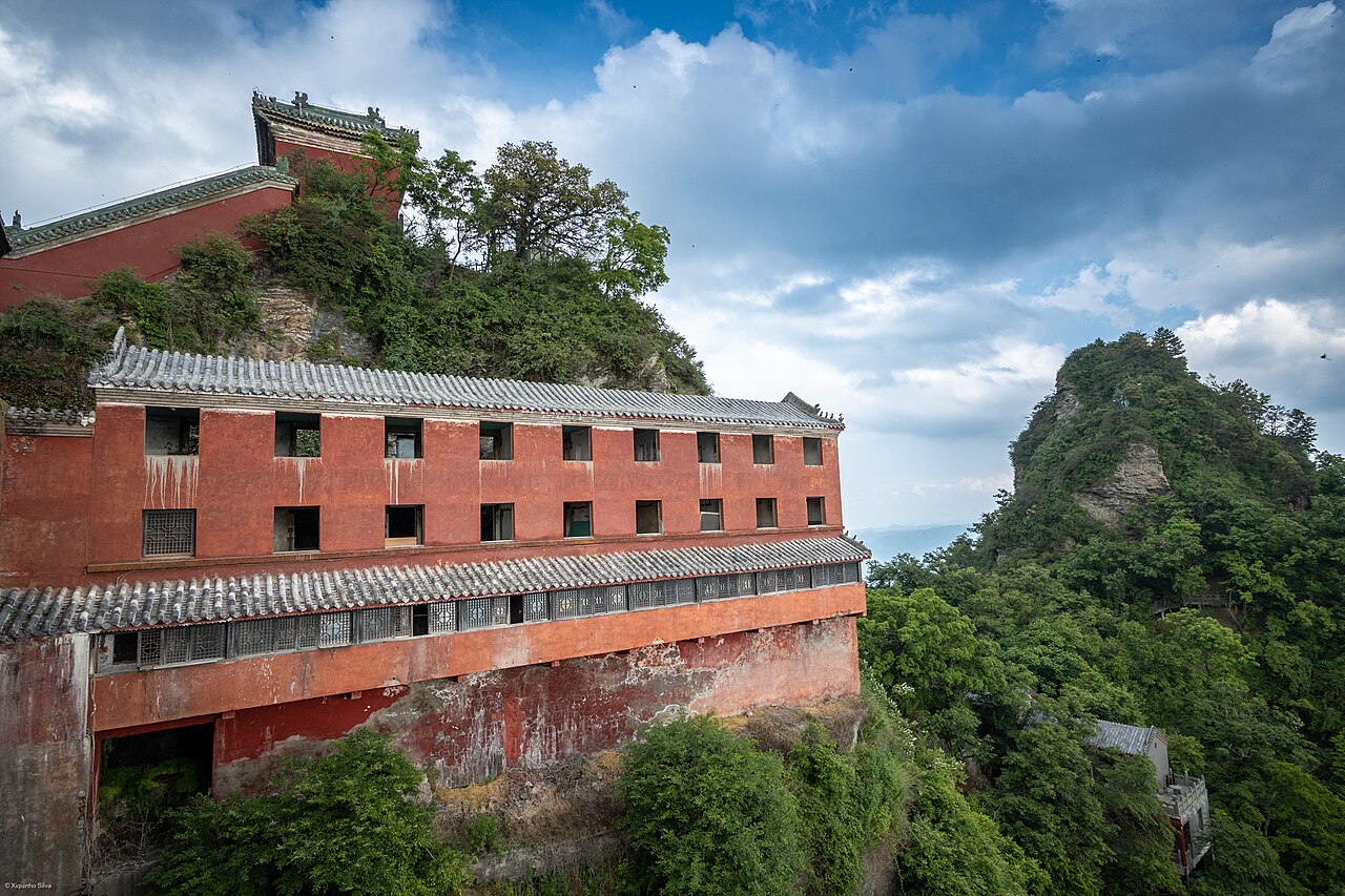 Temple complex buildings on rocky cloud-shrouded peaks of the Wudang Mountains with precipitous forested cliffs below, Hubei Province, China