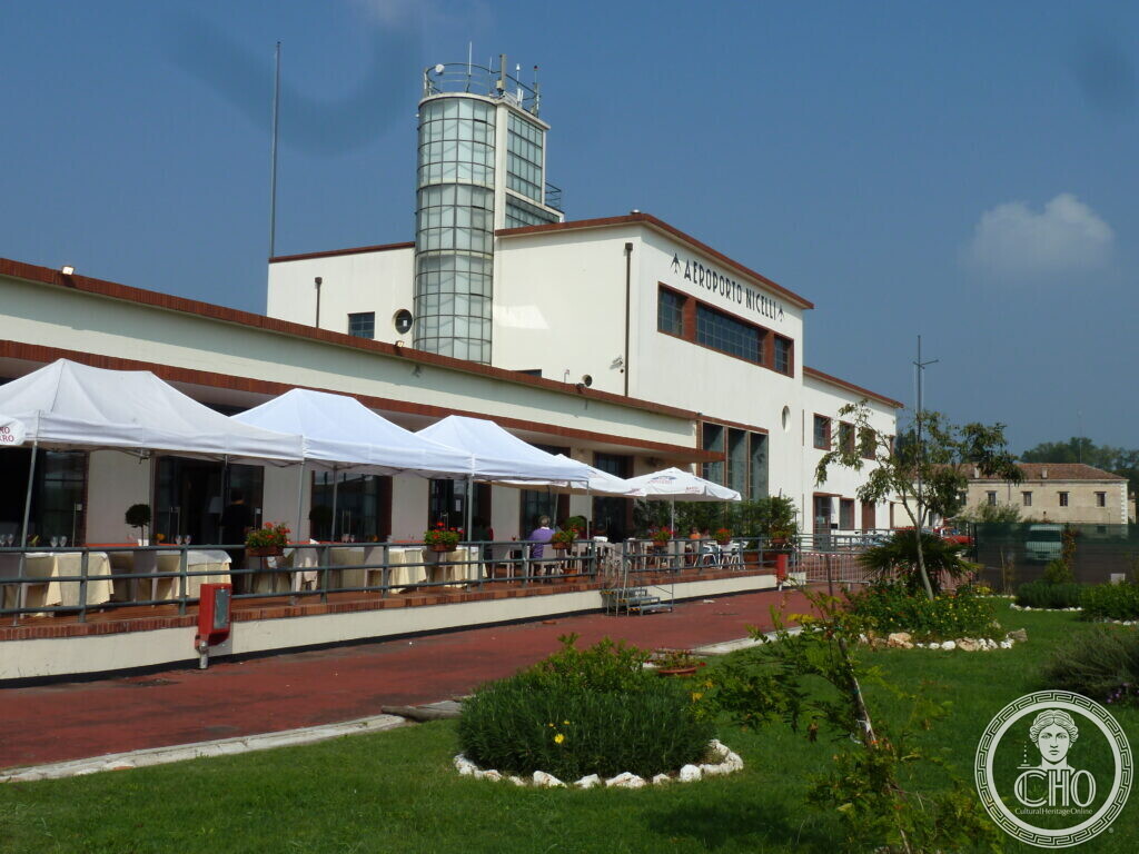 Front facade of Nicelli airport terminal on the Lido di Venezia, with the AEROPORTO NICELLI sign and the cylindrical glass control tower