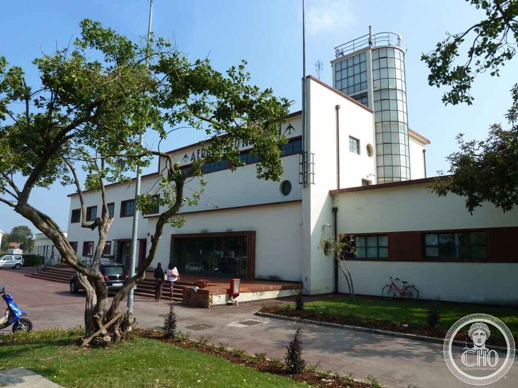 The entrance front of Nicelli airport terminal with its sign, tower and forecourt trees