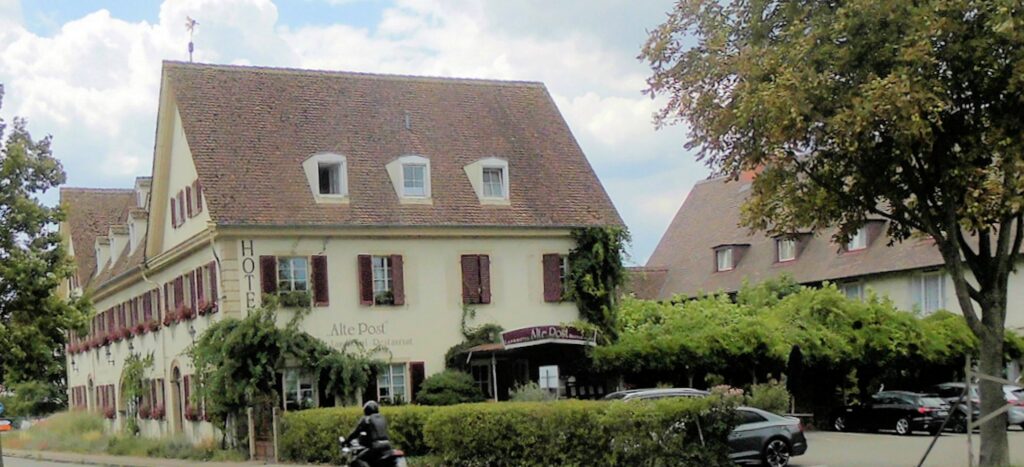 Long cream coaching inn with steep tiled roof, wine-red shutters and climbing vines, Müllheim