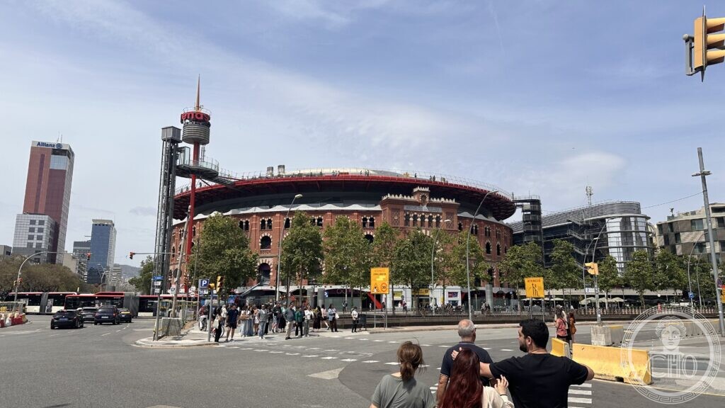 Wide view of Arenas de Barcelona from the Gran Via intersection, with the Allianz tower and Barcelona's skyline behind