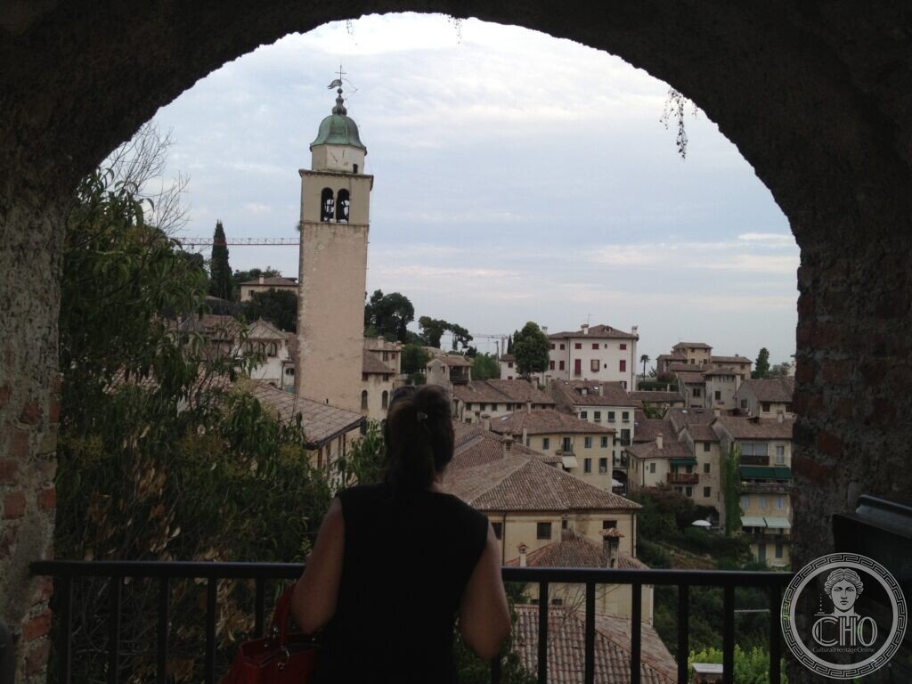 View of Asolo rooftops and a bell tower framed by a stone archway of the castle