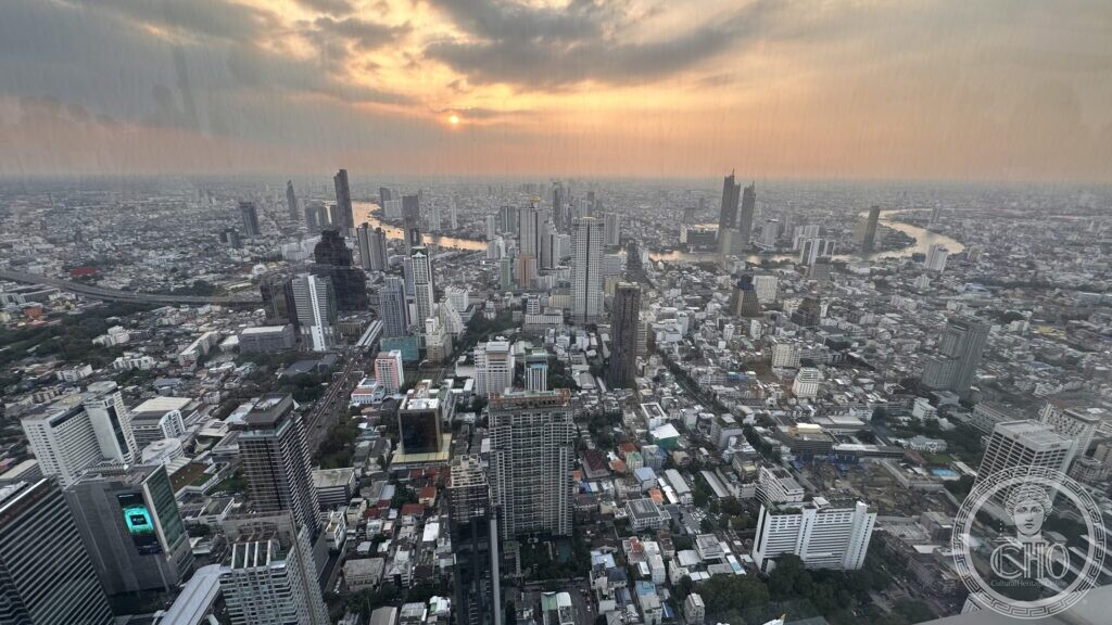 Bangkok seen at sunset from a high observation deck, the Chao Phraya river winding through a horizon-wide field of towers and low roofs