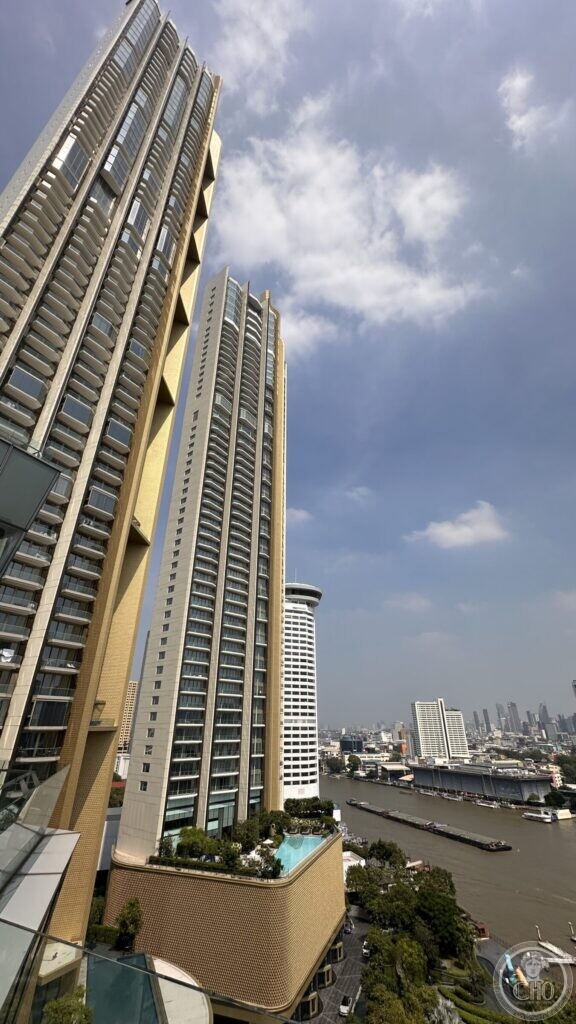 Residential towers with planted terraces rising above the Chao Phraya, with a barge on the river and the low city beyond