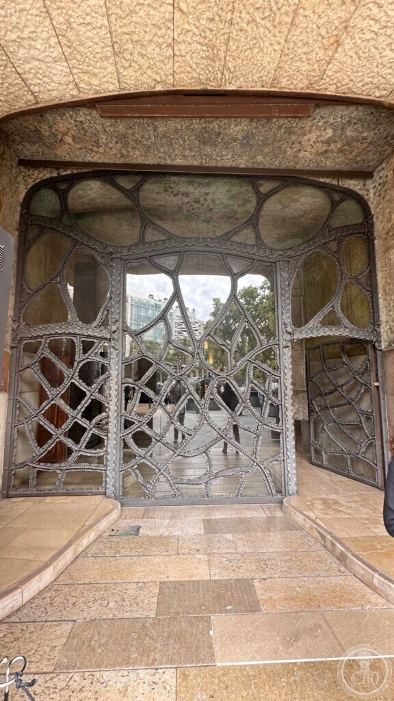 A large iron gate of irregular cells and organic tracery, under a rough stone lintel