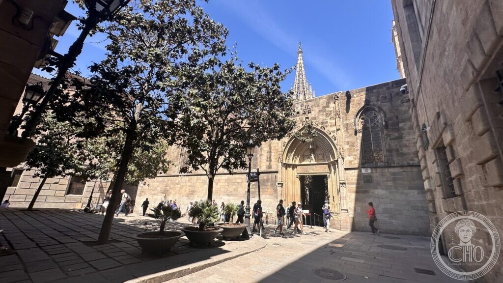 A Gothic doorway in a stone wall with the cathedral spire behind and trees in planters