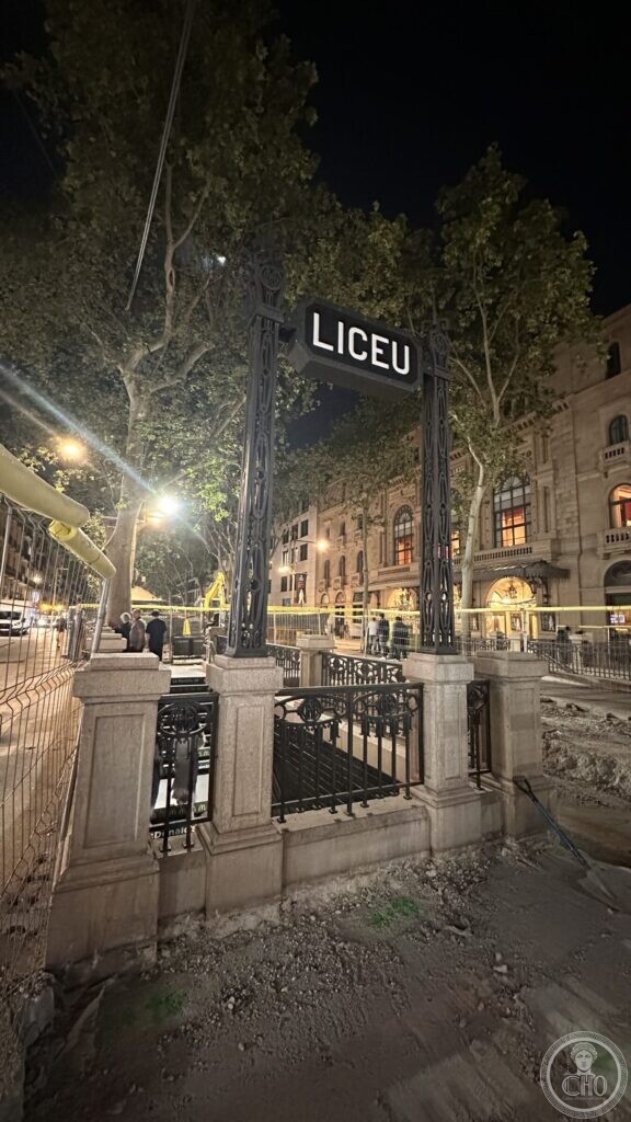A wrought-iron metro entrance frame lettered LICEU, at night, with the opera house behind