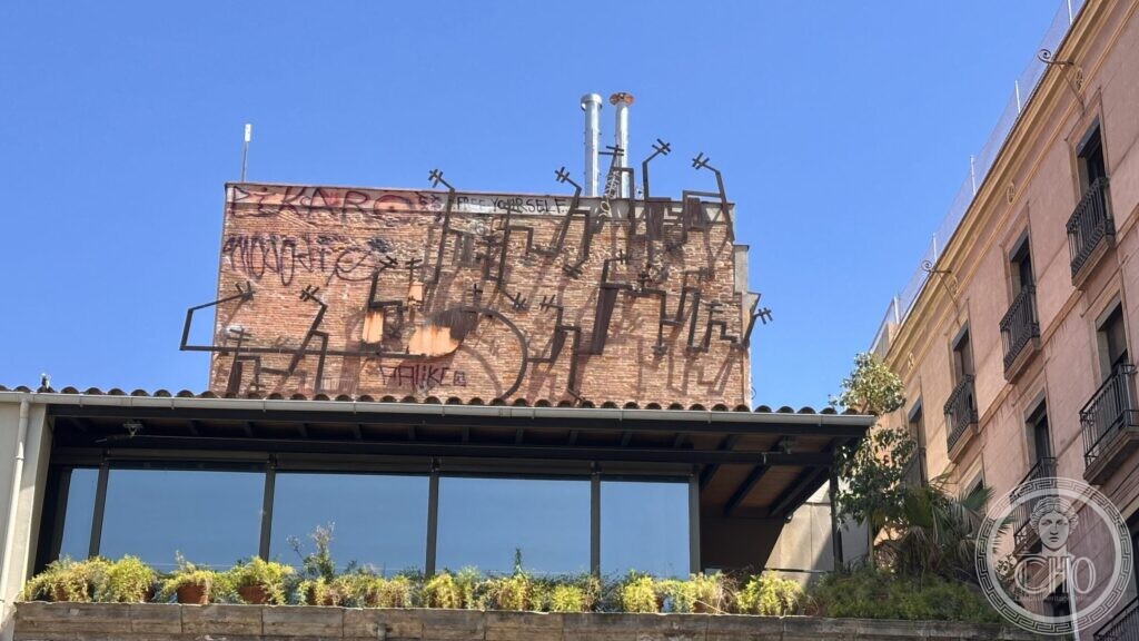 A brick party wall above a glazed terrace near the museum, carrying old iron brackets and graffiti