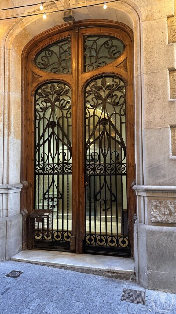 A tall wooden door on Passeig de Gràcia with curling wrought-iron grilles and a fanlight of iron stems